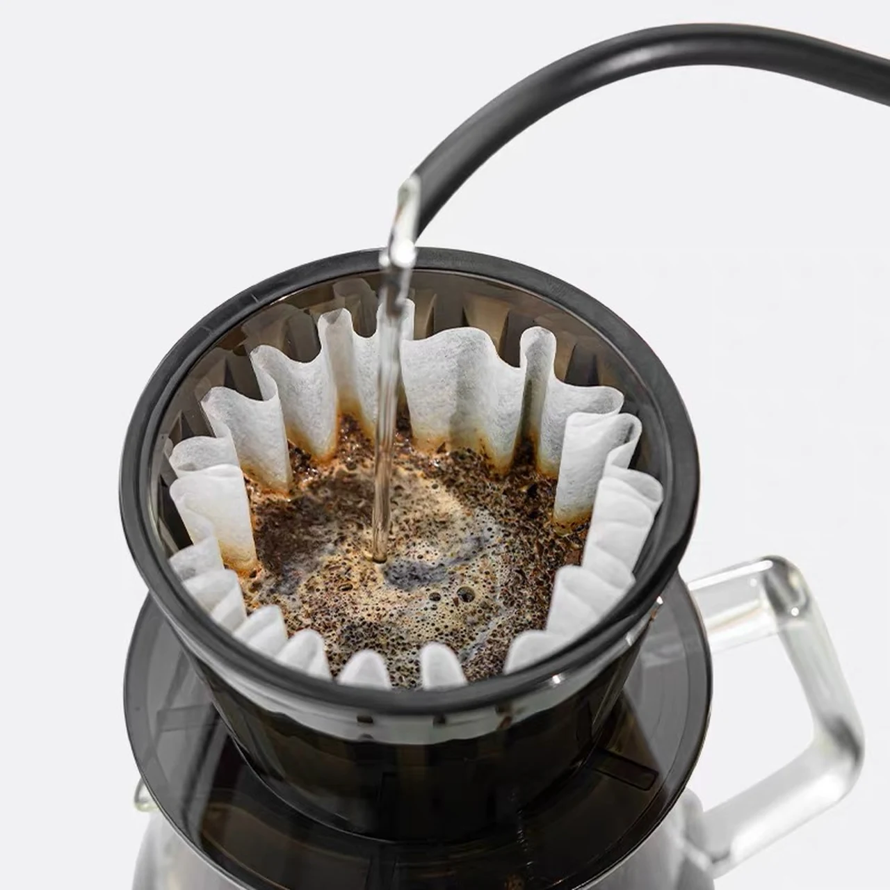 Water being poured into a white pleated basket coffee filter in a dripper.