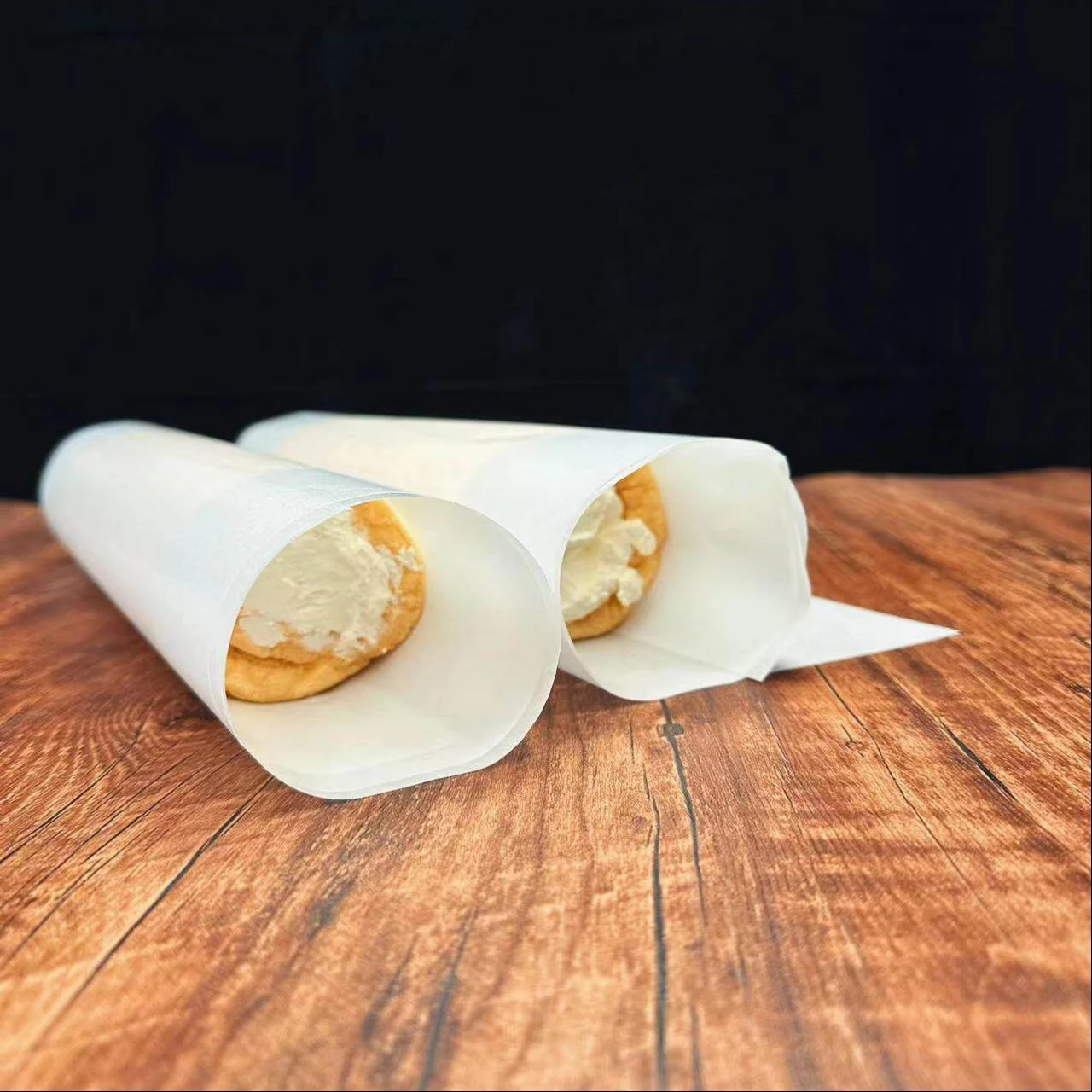 Food wrapped in white baking paper on a wooden surface.