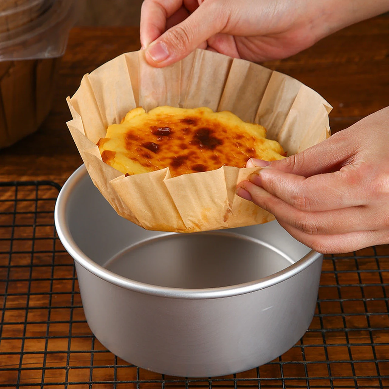 Mains soulevant un gâteau basque d'un moule métallique à l'aide de sa chemise en papier de couleur naturelle.