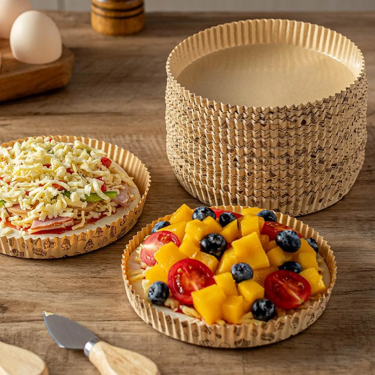 Plateaux à pizza imprimés empilés près de plateaux garnis d'ingrédients salés et de fruits.