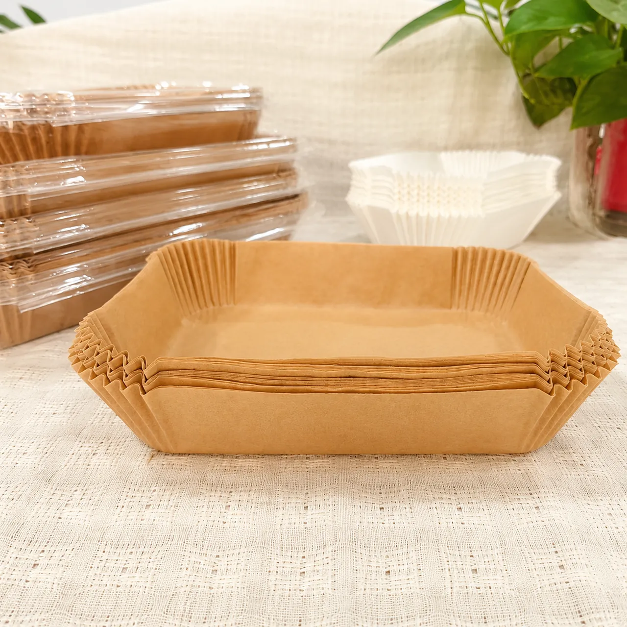 Stacked rectangular air fryer liners on a table beside packaged liners and white liners.