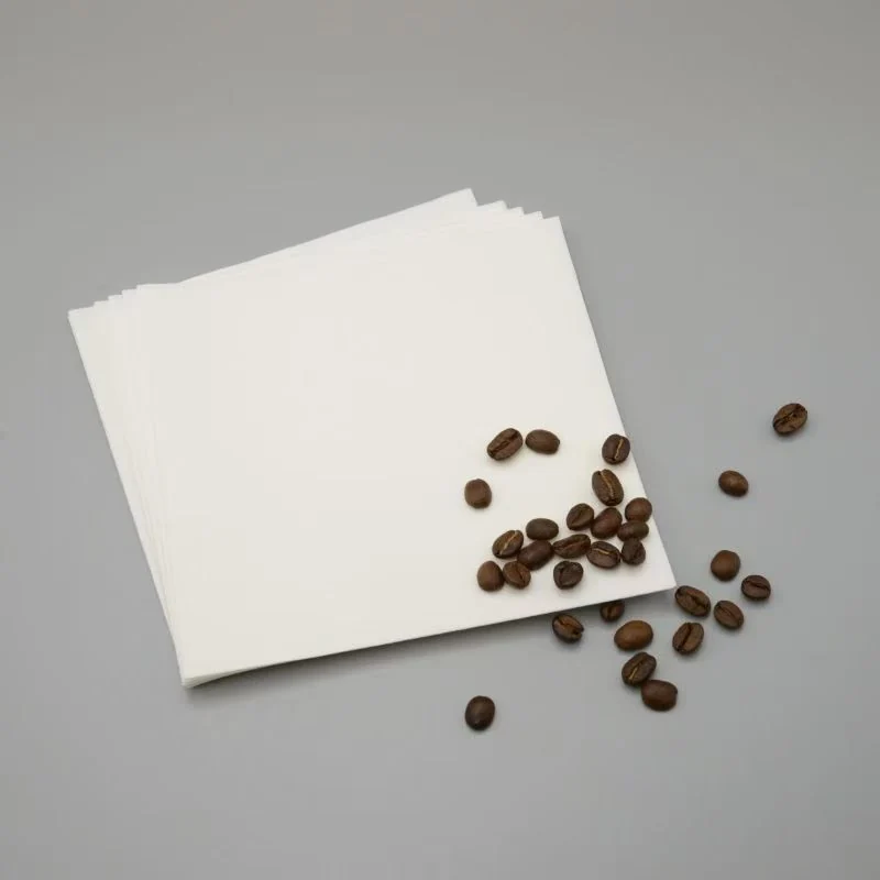 White folded square coffee filters beside coffee beans.
