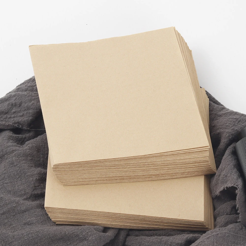Stack of brown square coffee filters on grey fabric.