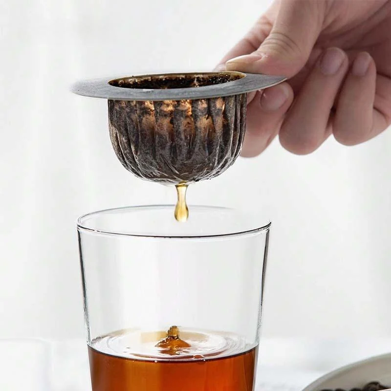 A hand holding a round support filter as coffee drips into a glass.